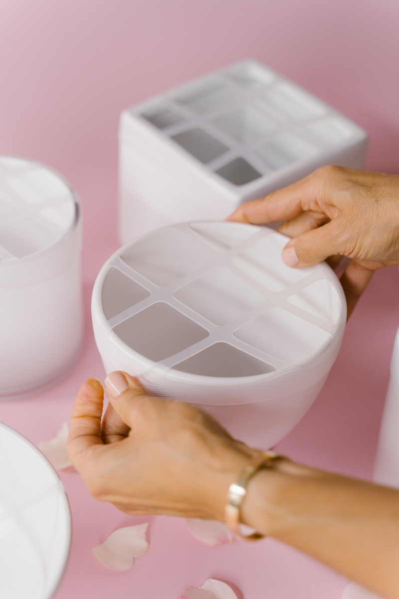 Hands placing Blossom Grid on a white vase with a pink background.