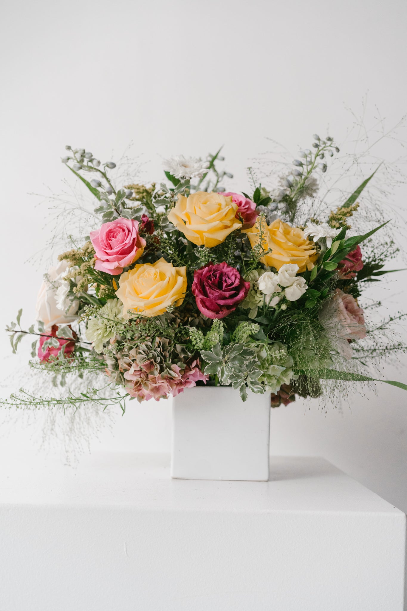 Floral arrangement using Blossom Grid with pink, yellow, and red flowers in a white container on a white background
